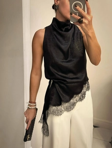 Detail of black satin halter top featuring a draped neckline and eyelash lace hemline