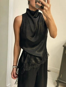 Detailed close-up of glossy black satin halter top with elegant lace hem and asymmetrical cut
