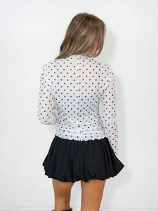 Back view of a white polka dot mesh long sleeve top with a black pleated skirt for women