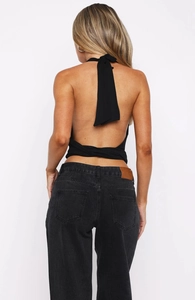 Detail view of a black backless halter top with ties and high-waisted denim jeans