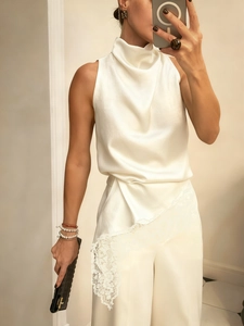 Detail of white satin sleeveless top with cowl neck and lace patchwork hem pants