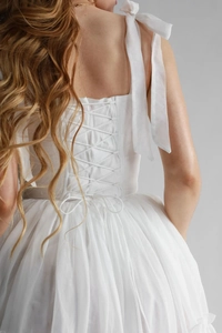Détail d'une robe corset blanche avec laçage au dos et bretelles ornées de nœuds rubans