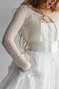 Gros plan du boléro en dentelle blanche avec textures florales et rubans élégants
