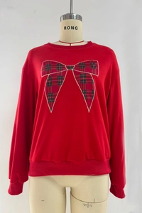 Detail of red crewneck sweatshirt featuring a plaid bow patch with white embroidery