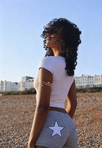 Close-up of star print striped denim shorts and gold arm cuff against a coastal background