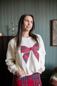 Detail of a beige sweatshirt with a large red tartan plaid bow on a female model