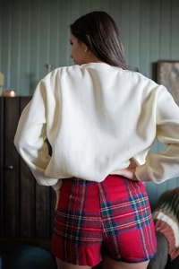 Rear view of cream crew neck sweatshirt and red plaid shorts on a female model