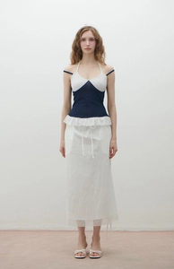 Detail of slim fit polka dot halter top with ruffle hem and layered white maxi skirt