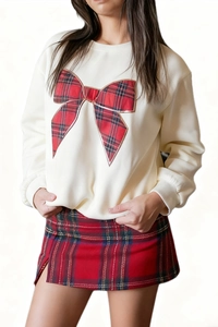Close-up of white round neck sweatshirt featuring a large red plaid bow and side-slit skirt