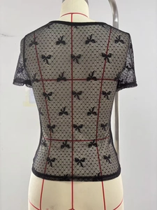 Détail d'un haut en maille noire avec des pois en dentelle et de petits nœuds en ruban