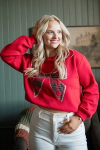 Detail of red crewneck sweatshirt featuring a large festive plaid bow and ribbed cuffs