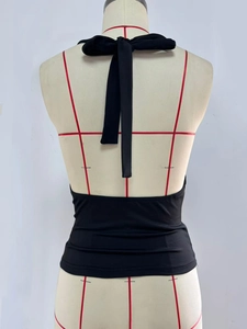 Detail of a black halter neck backless crop top featuring wide adjustable fabric ties
