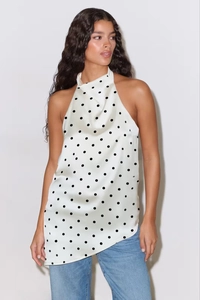 Detail of white polka dot halter neck top with sleek satin texture and irregular hemline