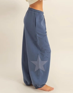 Detail of blue-grey joggers featuring three star patches and elastic drawstring waist