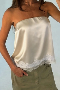 Detail of champagne satin tube top featuring delicate white eyelash lace hem trim