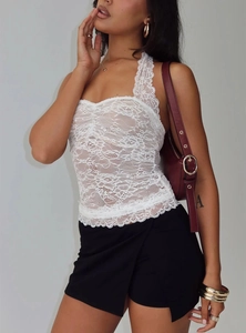 Detail shot of white lace halter top featuring floral embroidery and wavy hemline