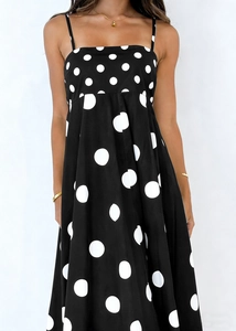 Detail of black summer dress with white polka dots, featuring thin shoulder straps
