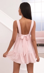 Detailed back view of a pink backless dress featuring a large bow and ruffled hemline