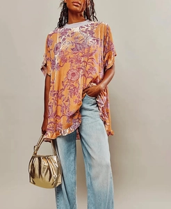 Detail of velvet floral top with ruffled hem paired with blue jeans and a gold handbag