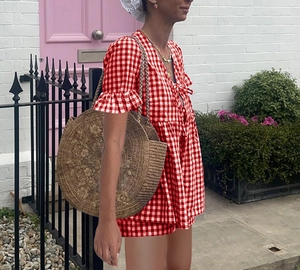 Détail du haut à carreaux vichy rouge avec nœud et un grand sac en paille tressée