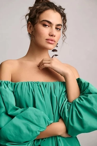 Detail of emerald green off-shoulder dress featuring puffy lantern sleeves and pleated fabric