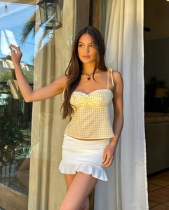 Detail of yellow gingham lace-up camisole and white knit ruffle skirt on a model