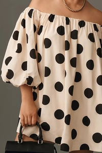 Detail of off-shoulder neckline and puff sleeves on a beige polka dot dress