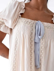 Détail de manches bouffantes beiges avec dentelle et petit nœud en ruban bleu