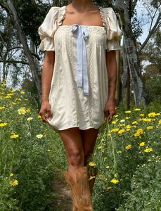 Détail de mini-robe beige à col carré avec nœud bleu et finitions en dentelle fine