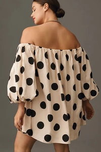 Detail of off-shoulder puff sleeves on cream-colored dress with bold black polka dots