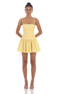 Détail d'une mini robe jaune clair froncée avec bretelles nouées et jupe plissée évasée