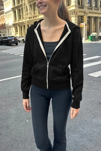 Detail of a black zip-up hoodie featuring a contrasting white zipper and side pockets