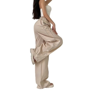 Detail of loose-fit beige trousers featuring white side stripes and drawstring waist