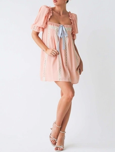 Détail de la mini robe rose clair avec manches bouffantes, dentelle et nœud en soie bleu