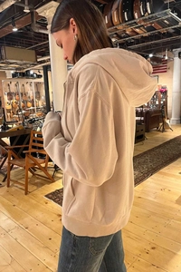 Detail of beige zip-up hoodie featuring a spacious hood and loose fit on a model
