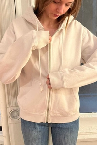 Detail of cream zip-up hoodie featuring matching drawstrings and a smooth metal zipper