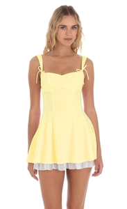 Détail d'une mini-robe jaune clair avec bretelles à nœuds et ourlet plissé blanc contrasté