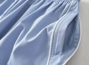 Close-up of light blue sporty pants featuring white side stripes and seamless pocket details