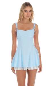 Détail de robe mini bleu clair avec bretelles à nœuds et ourlet plissé blanc