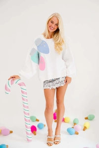 Detail of white Christmas sweatshirt featuring colorful sequin bulb patches and stars