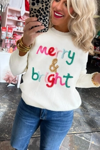 Detail of white knit sweater featuring colorful chenille merry and bright embroidery