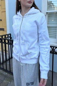 Detail of white zip-up hoodie featuring a drawstring hood and metallic zipper closure