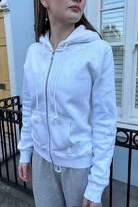 Outdoor street style view of a white zip-up hoodie with front pockets and drawstrings
