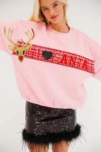 Close-up of pink Christmas sweatshirt with sequined deer pattern and black feathered skirt