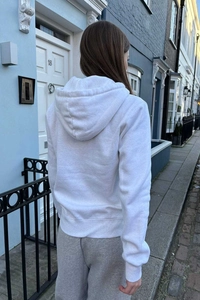 Outdoor street view of the white zip-up hoodie and grey joggers from a back perspective