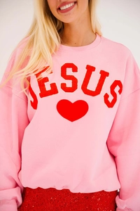 Detail of red chenille JESUS lettering and heart patch on hot pink crewneck sweatshirt