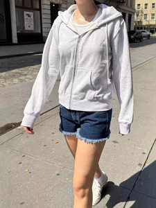 Women's casual grey zip-up hoodie paired with distressed denim shorts for spring style