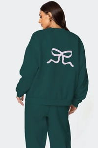 Détail d'un sweat vert foncé avec un grand imprimé nœud rose dessiné à la main au dos