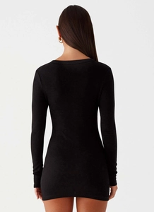 Rear view of a black slim-fit ribbed knit long-sleeve mini dress on a model