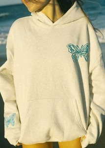 Detail of blue butterfly embroidery on loose oatmeal hoodie with a kangaroo pocket